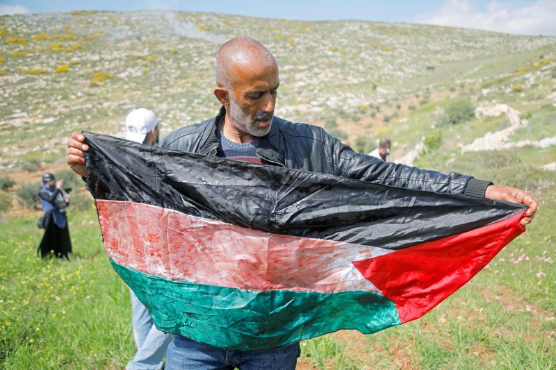 Un hombre sostiene una bandera palestina manchada de sangre de un palestino herido de muerte durante una protesta contra los asentamientos israelíes, en Beit Dajan, en Cisjordania,